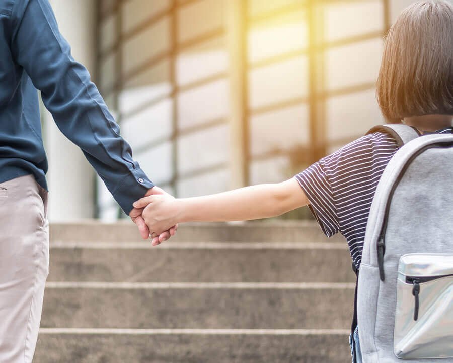 Un enfant avec un cartable tenant la main d'un adulte.