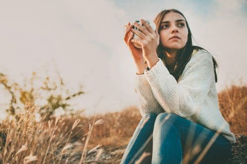 Une jeune fille dehors buvant un café.